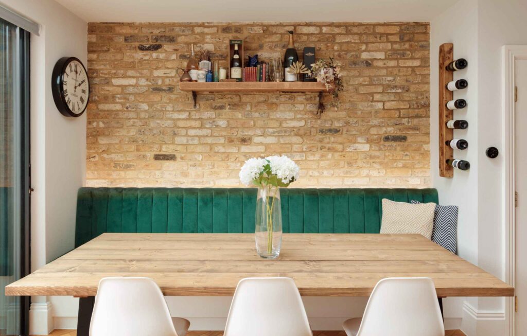 A table with white chairs and a vase of flowers in front of a brick wall